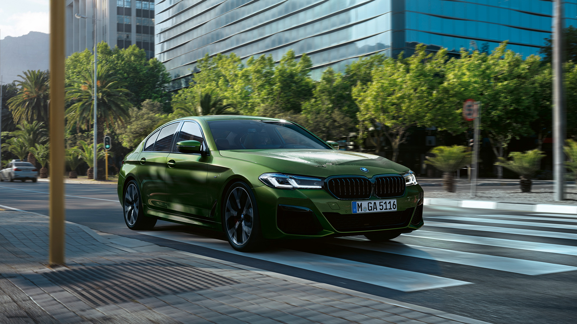 BMW M550i xDrive Sedan G30 LCI Facelift 2020 tříčtvrteční pohled zepředu při jízdě BMW M550i xDrive Sedan G30 LCI Facelift 2020 v metalické barvě BMW Invidividual Verde Ermes (zelená) ze tříčtvrtečního pohledu zepředu při jízdě centrem města