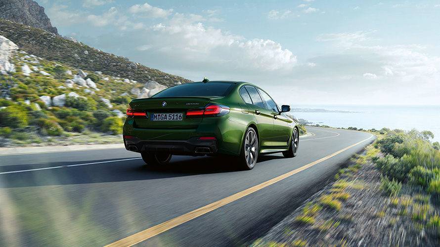 BMW M550i xDrive Sedan G30 LCI Facelift 2020 v metalické barvě BMW Invidividual Verde Ermes (zelená) ze tříčtvrtečního pohledu zezadu při jízdě
