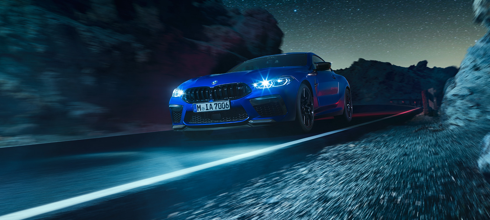 BMW M8 Competition Coupé, tříčtvrteční pohled zpředu. BMW M8 Competition Coupé v barvě Marina Bay Blue, tříčtvrteční pohled zpředu, za jízdy v noci.