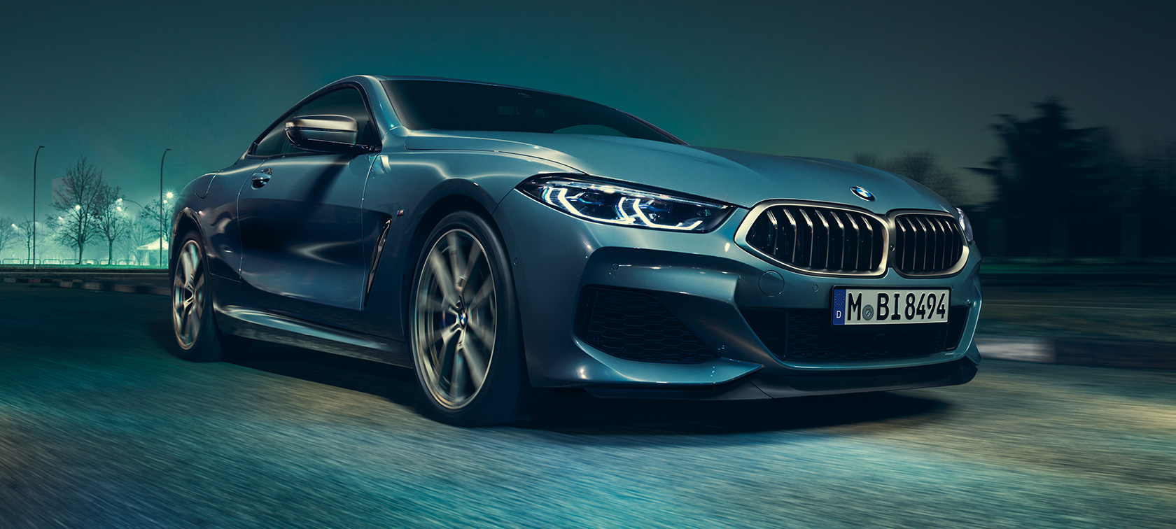 BMW M850i xDrive Coupé, tříčtvrteční pohled zepředu. BMW M850i xDrive Coupé v metalické barvě Barcelona Blue, tříčtvrteční pohled zepředu za jízdy.