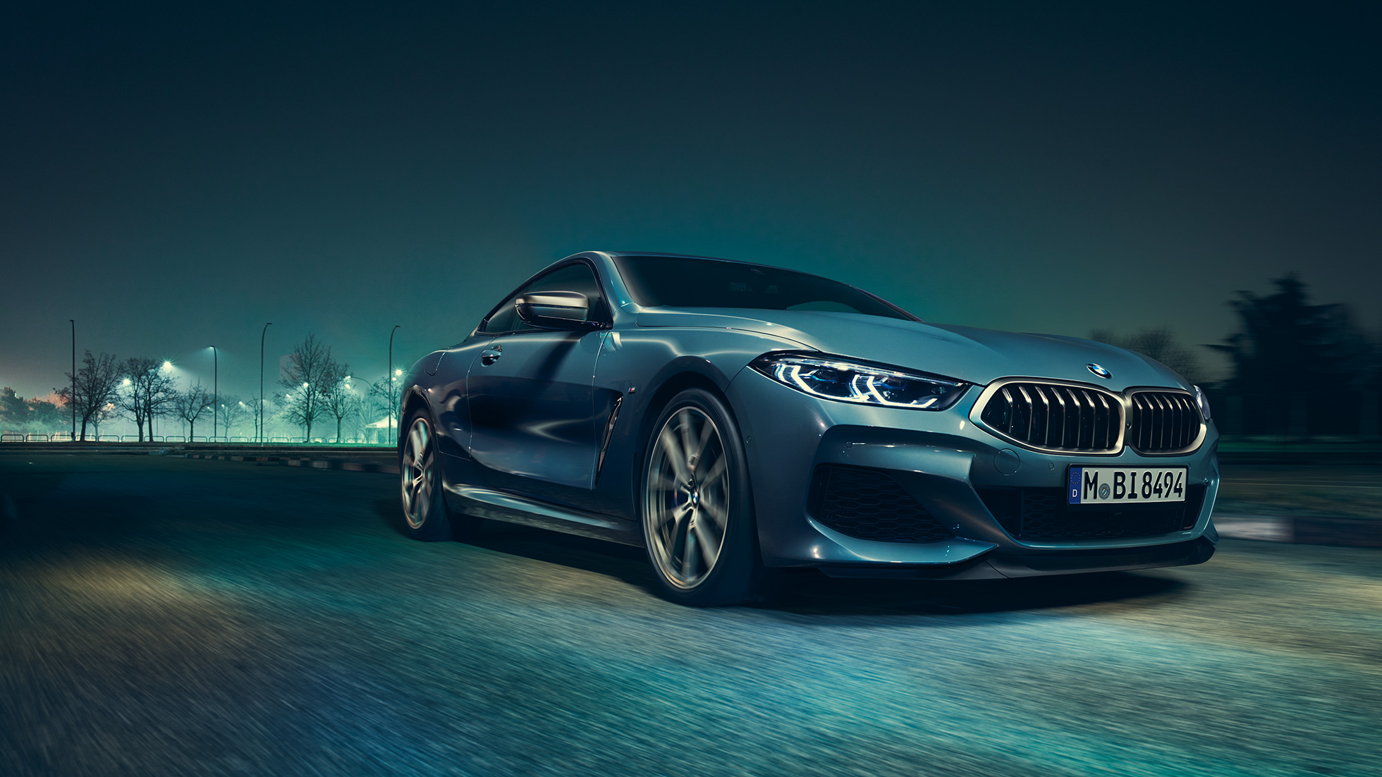 BMW M850i xDrive Coupé, tříčtvrteční pohled zleva za jízdy. BMW M850i xDrive Coupé v metalické barvě Barcelona Blue, tříčtvrteční pohled zleva, za jízdy v noci.