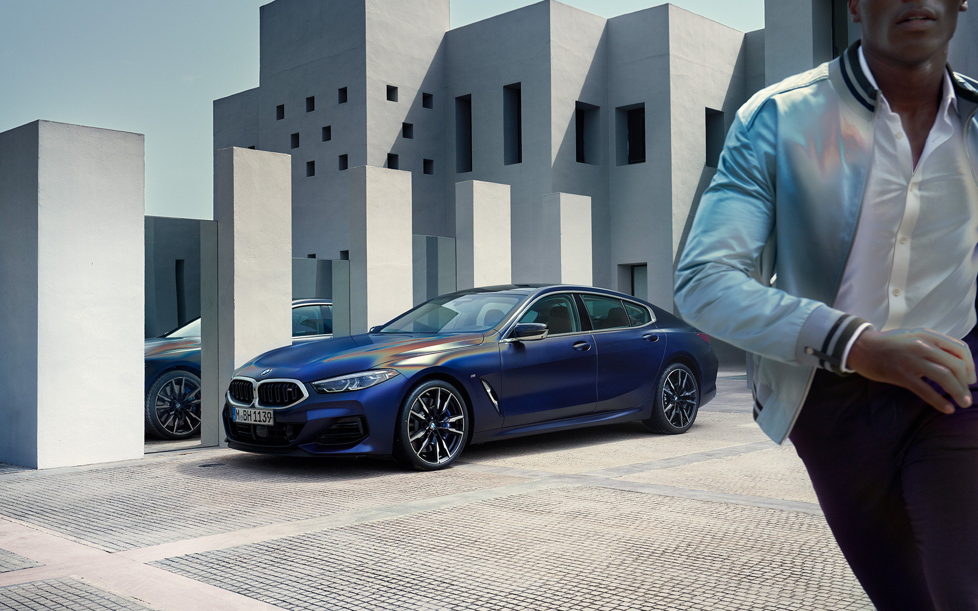 Tříčtvrteční pohled zepředu BMW M850i xDrive Gran Coupé G16 LCI Facelift 2022 BMW M850i xDrive Gran Coupé G16 LCI Facelift 2022 v metalické barvě BMW Invidividual Frozen Tanzanite Blue (modrá) ze tříčtvrtečního pohledu zepředu staticky s mužským modelem v popředí
