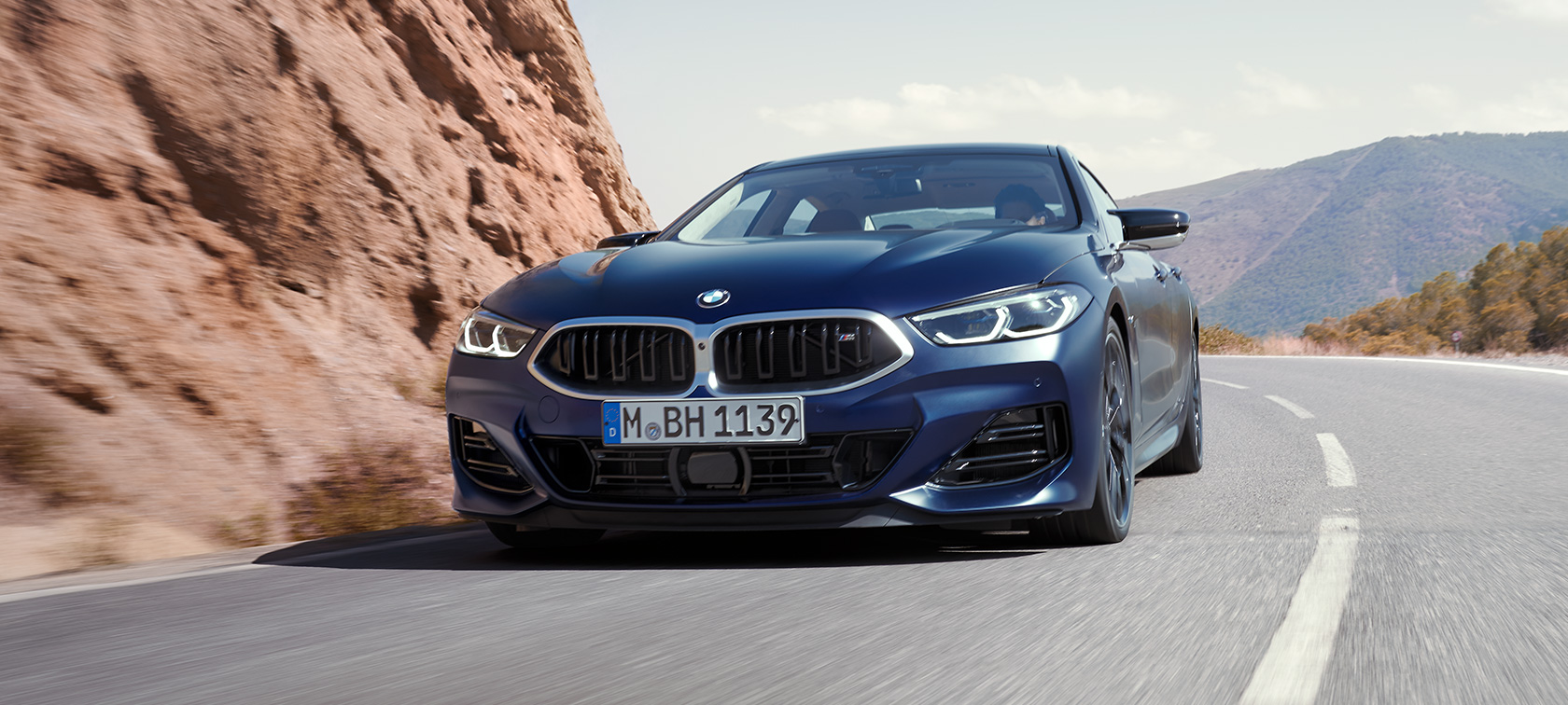 Tříčtvrteční pohled zepředu při jízdě BMW M850i xDrive Gran Coupé G16 LCI Facelift 2022 BMW M850i xDrive Gran Coupé G16 LCI Facelift v metalické barvě 2022 BMW Invidividual Frozen Tanzanite Blue (modrá) ze tříčtvrtečního pohledu zezadu při jízdě zatáčkou
