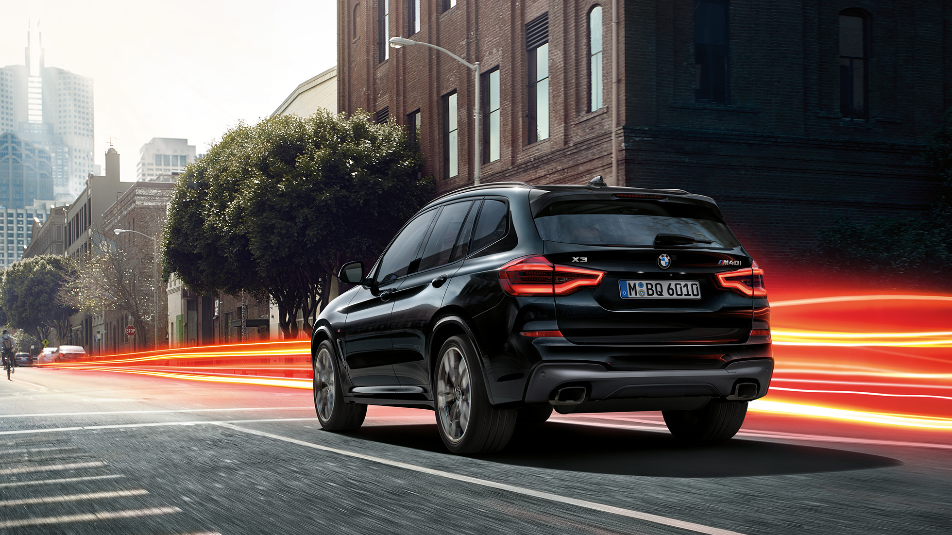 BMW X3 M40i v černé metalické barvě Black Sapphire, tříčtvrteční pohled zezadu. BMW X3 M40i v černé metalické barvě Black Sapphire, jízda, exteriér, tříčtvrteční pohled zezadu v městském prostředí se světelnými proužky.