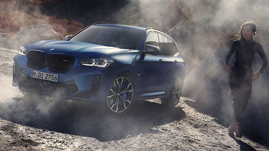 BMW X3 M Competition F97 LCI Facelift 2021 tříčtvrteční pohled zepředu staticky v kamenitém terénu BMW X3 M Competition F97 LCI Facelift 2021 v metalické barvě Frozen Marina Bay Blue (modrá) ze tříčtvrtečního pohledu v kamenitém terénu s modelkou