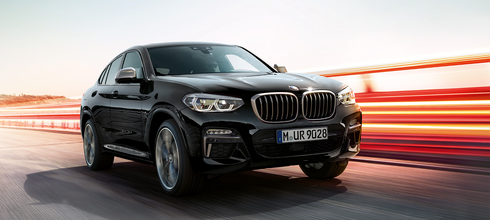 BMW X4 M40i a BMW X4 M40d, tříčtvrteční pohled zpředu, levá strana. BMW X4 M40i a BMW X4 M40d v černé metalické barvě Black Sapphire, exteriér, tříčtvrteční pohled zpředu, levá strana se světelnými proužky.