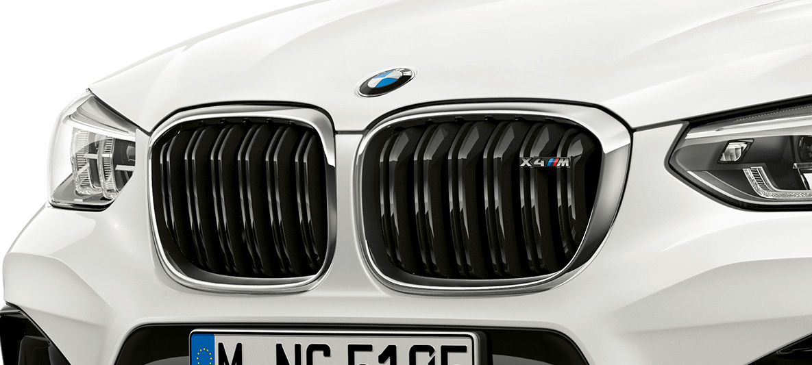 BMW X4 M v bílé barvě Alpine White, M maska chladiče ve tvaru ledvinek BMW X4 M v bílé barvě Alpine White, exteriér, přední část, M maska chladiče ve tvaru ledvinek s chromovými detaily a označením modelu.