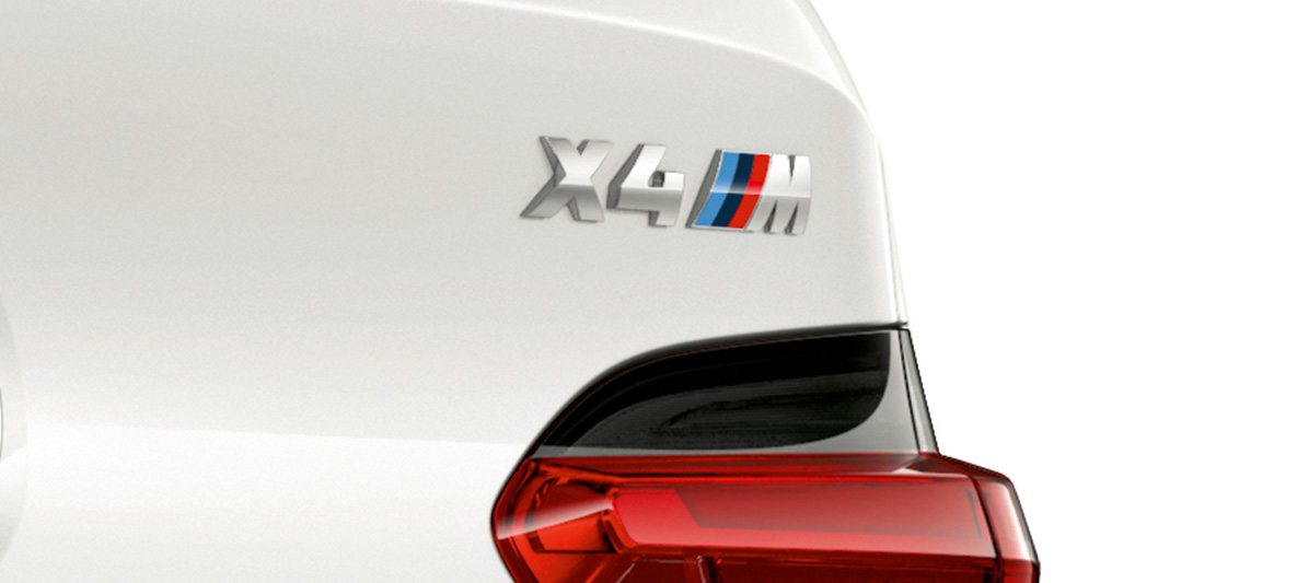 BMW X4 M, označení modelu. BMW X4 M v bílé barvě Alpine White, exteriér, detailní pohled na zadní část s označením modelu.