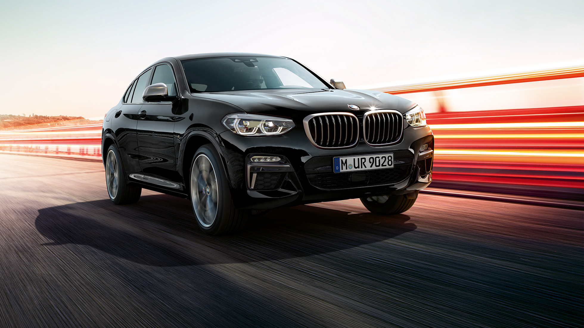 BMW X4 M40i a BMW X4 M40d, tříčtvrteční pohled zpředu. BMW X4 M40i a BMW X4 M40d v černé metalické barvě Black Sapphire, exteriér, tříčtvrteční pohled zpředu, levá strana se světelnými proužky.