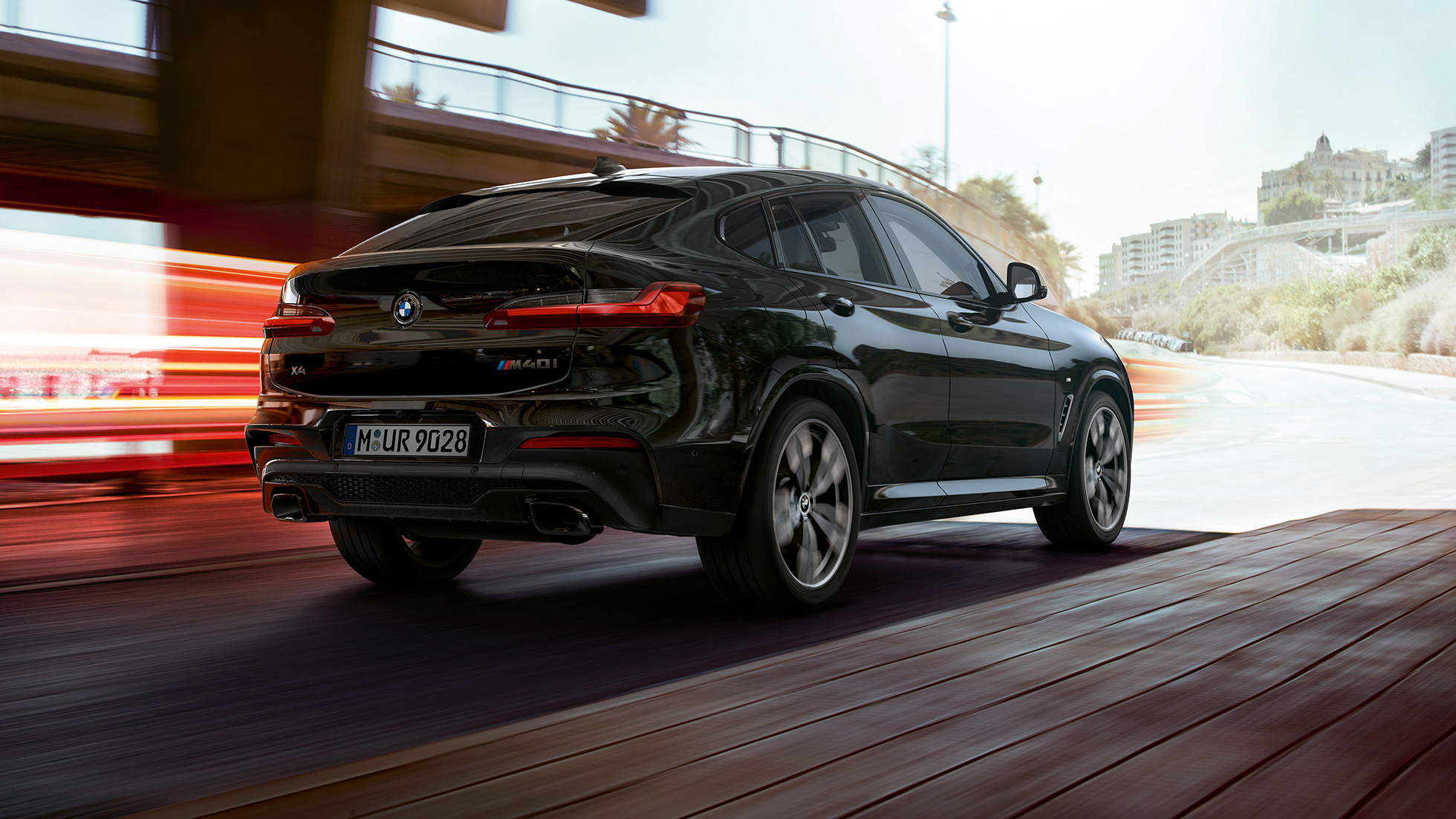 BMW X4 M40i, tříčtvrteční pohled zezadu. BMW X4 M40i v černé metalické barvě Black Sapphire, exteriér, tříčtvrteční pohled zezadu, levá strana se světelnými proužky.