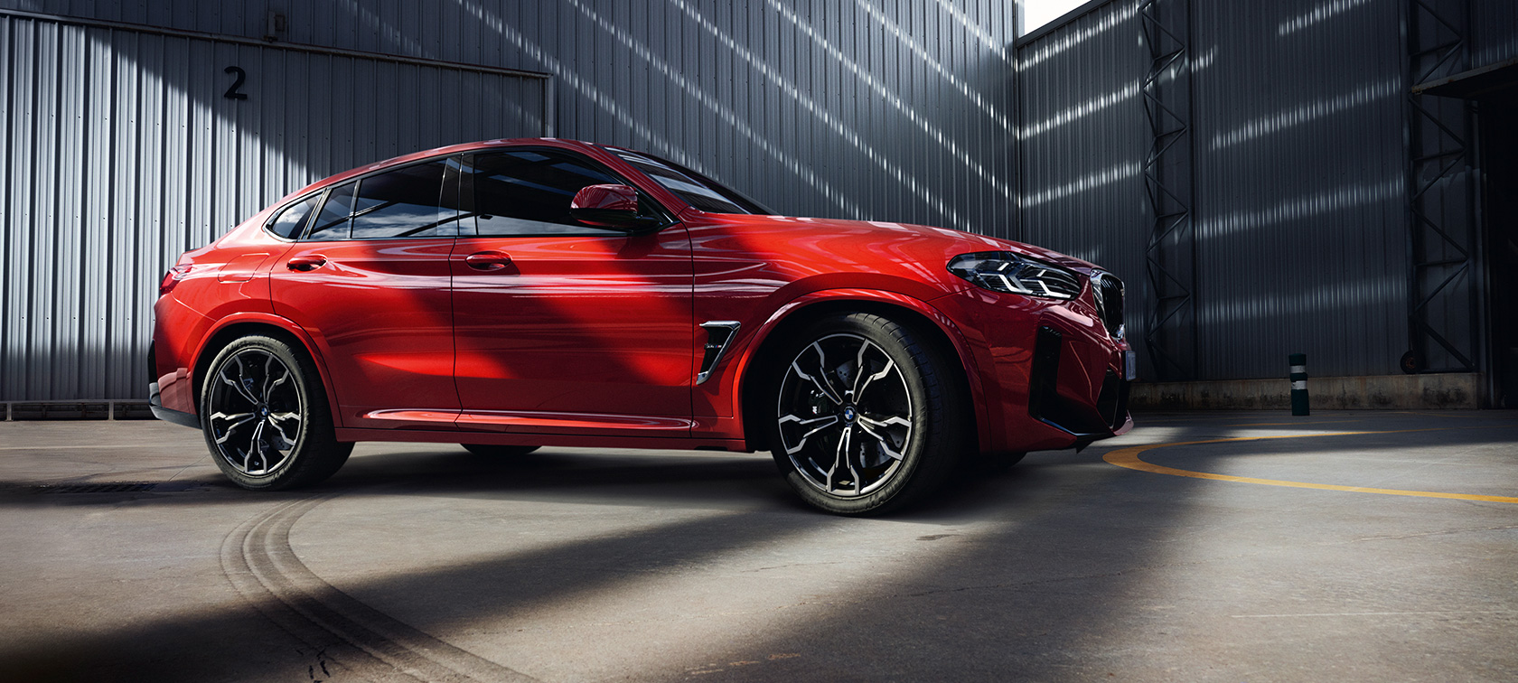 Tříčtvrteční pohled zepředu BMW X4 M F98 LCI Facelift 2021 BMW X4 M F98 LCI Facelift 2021 v metalické barvě Toronto Red (červená) z tříčtvrtečního pohledu zepředu v tovární budově