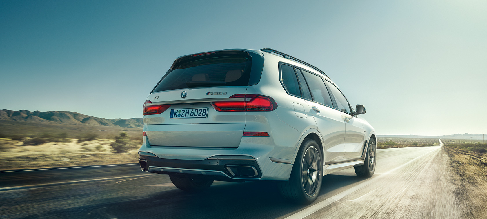 BMW X7 M50d, pohled zezadu BMW X7 M50d v bílé Mineral White, jedoucí na prázdné dálnici, pohled zezadu, G07, 2019