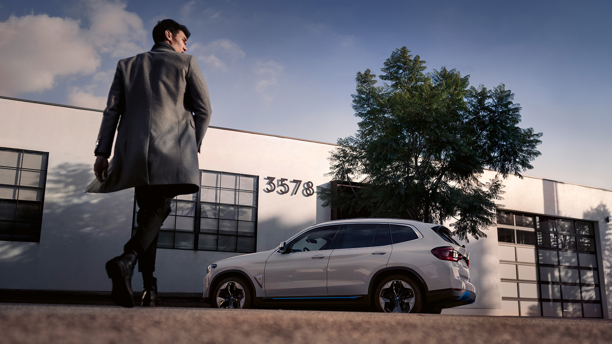 BMW iX3 G08 boční pohled před budovou s mužem BMW iX3 G08 2020 v metalické barvě Mineral White (bílá) boční pohled před budovou s mužem