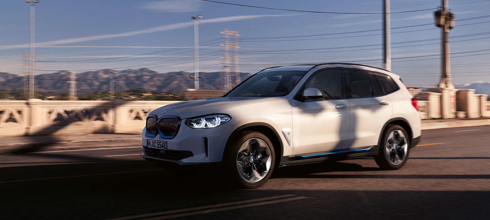 BMW iX3 G08, tříčtvrteční pohled zepředu, v jízdě na silnici BMW iX3 G08 2020 v metalické barvě Mineral White (bílá), tříčtvrteční pohled zepředu, v jízdě na silnici