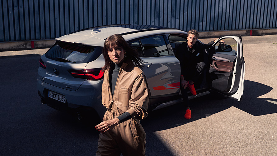 BMW X2 F39 Brooklyn Grey (šedá) tříčtvrteční pohledu zezadu s otevřenými dvěřmi a dvěma osobami BMW X2 F39 Brooklyn Grey (šedá) tříčtvrteční pohledu zezadu s otevřenými dvěřmi a dvěma osobami