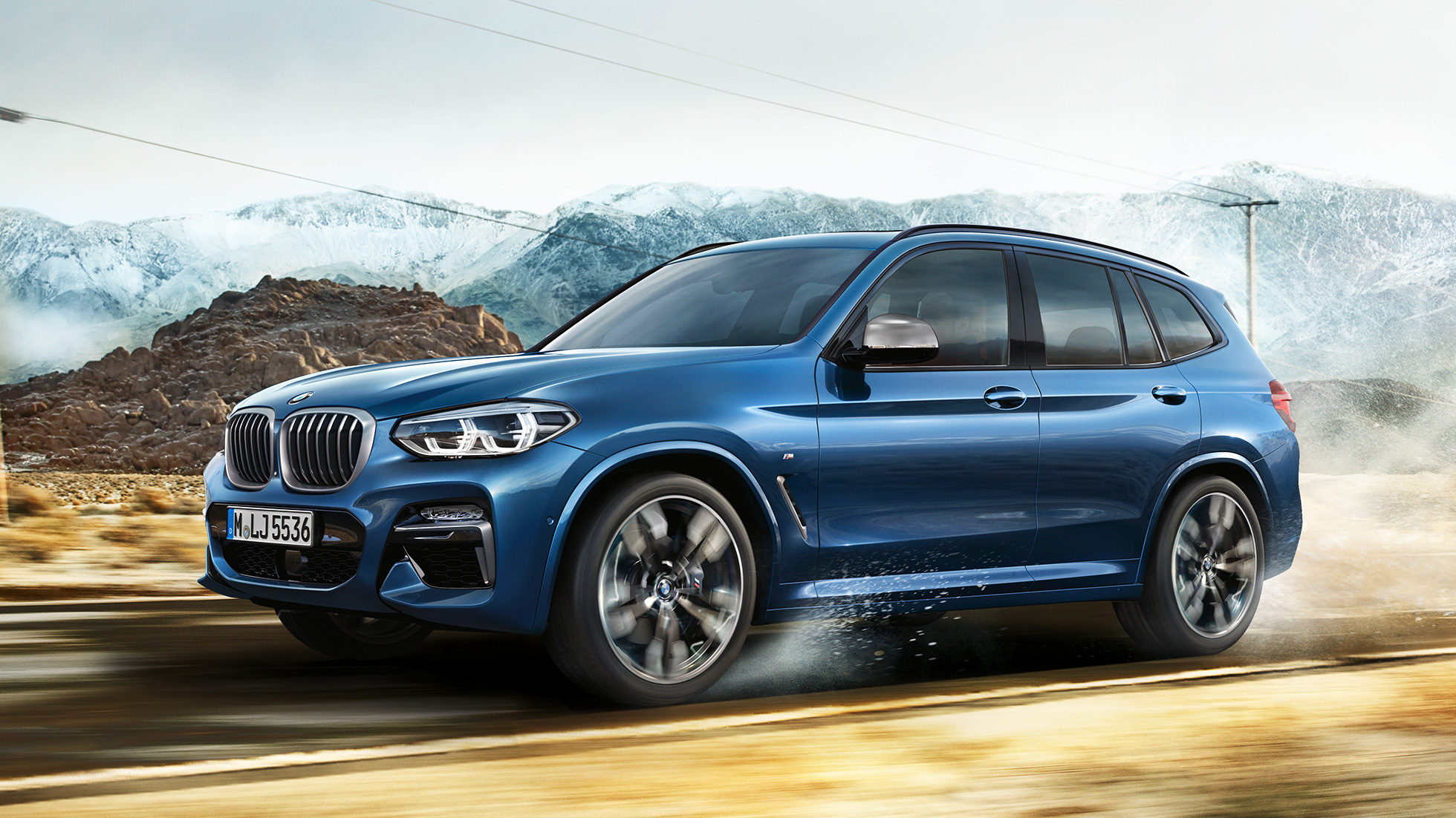 BMW X3 M40i, záběr na střední část kola a přední nárazník s horami v pozadí BMW X3 M40i, záběr na střední část kola a přední nárazník s horami v pozadí