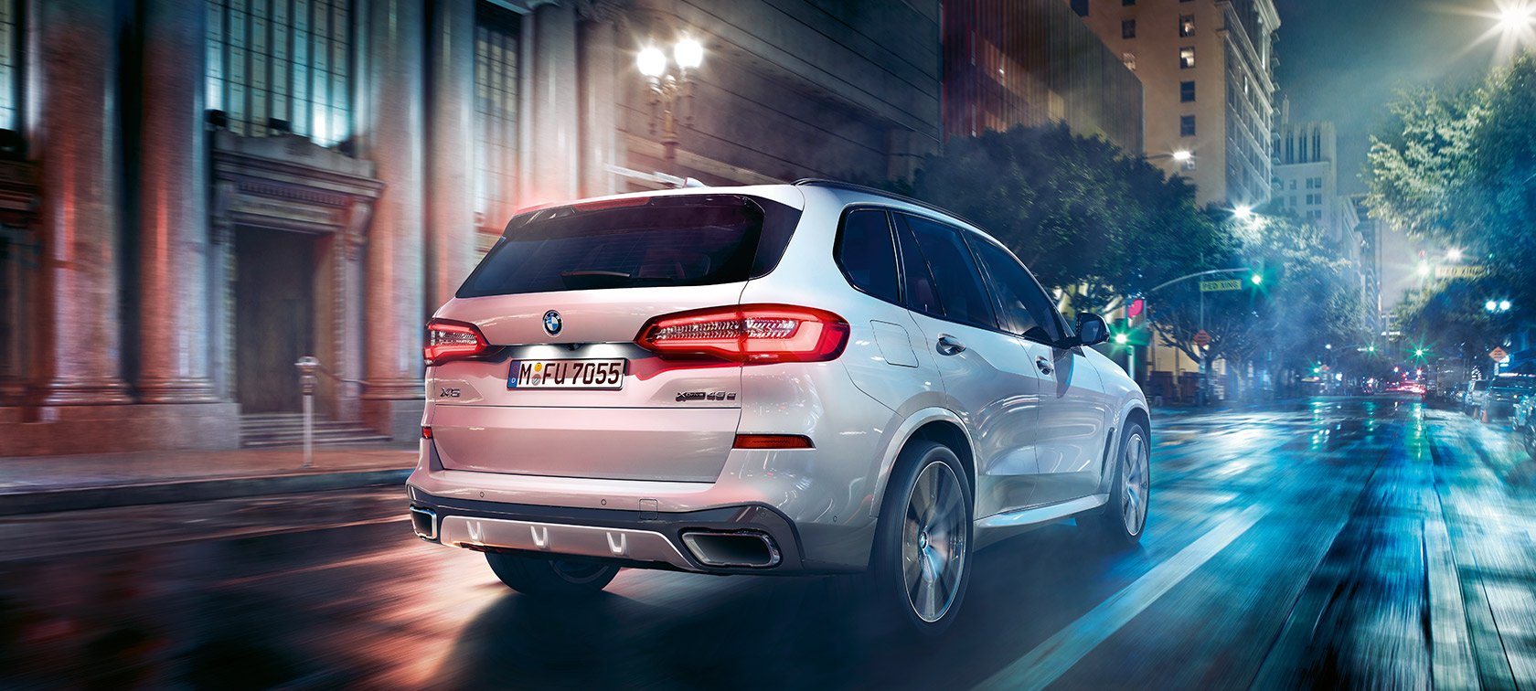 BMW X5 ze tříčtvrtečního pohledu zezadu při jízdě BMW X5 G05 2018 v metalické barvě Mineral White (bílá) z tříčtvrtečního pohledu zezadu při jízdě