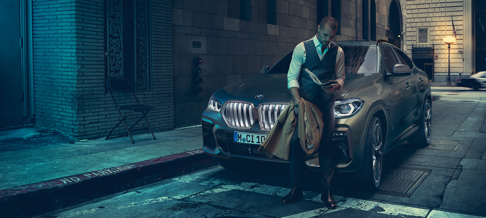 Muž se opírá BMW X6. Muž opírající se o BMW X6 při pohledu z boku před městským prostředím.