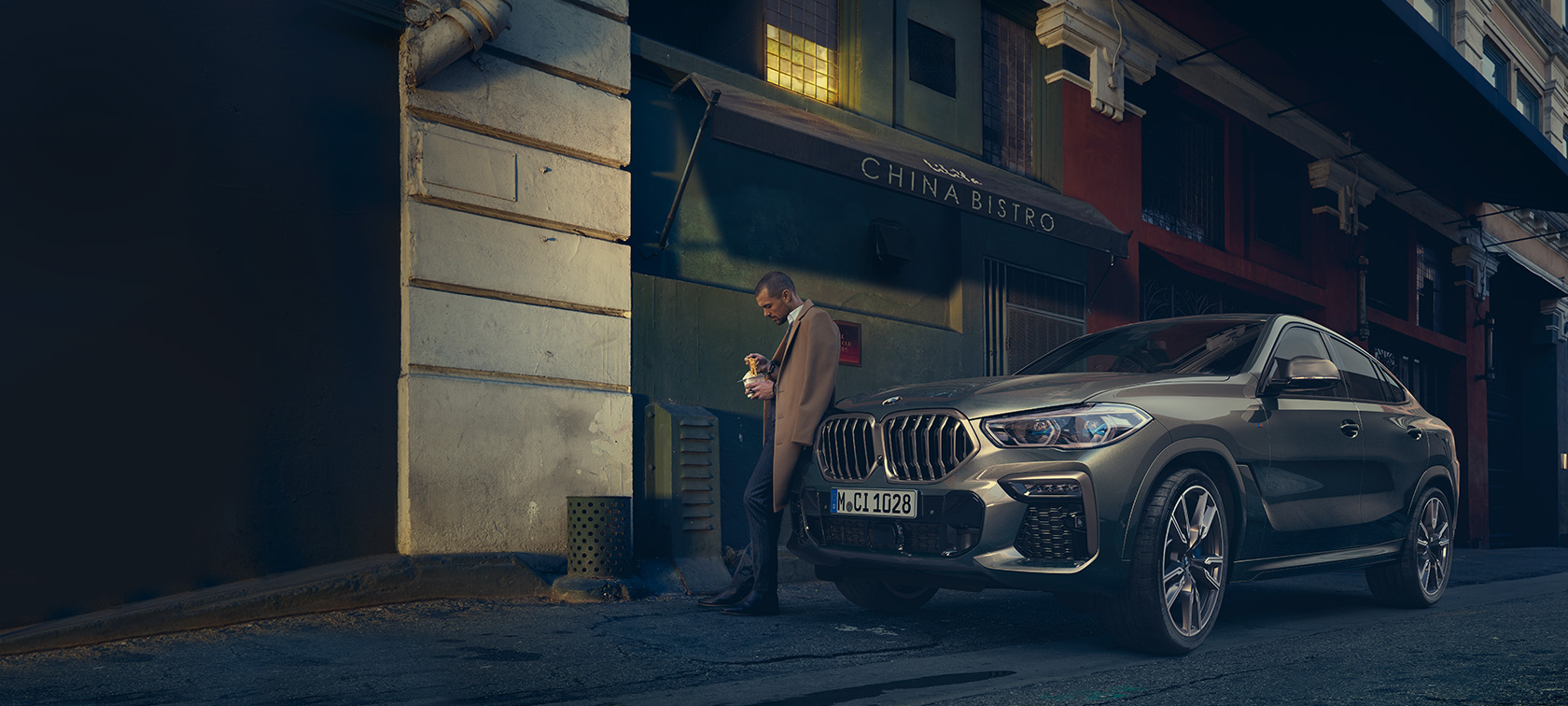 BMW X6 ze tříčtvrtečního pohledu zezadu při jízdě BMW X6 G06 2019 v metalické barvě Manhattan (zelená) z tříčtvrtečního pohledu zezadu při jízdě