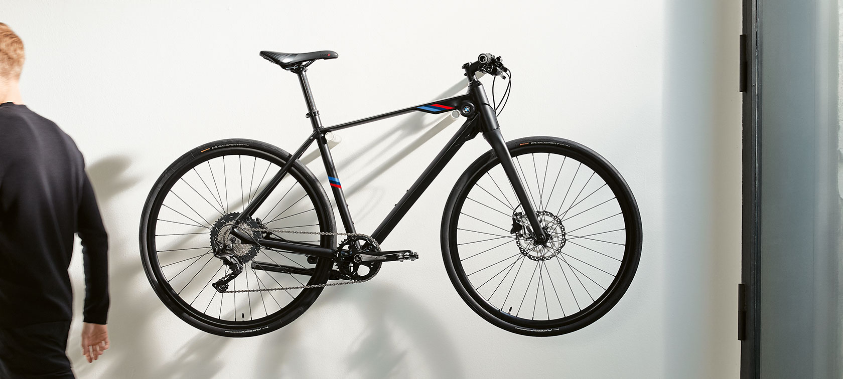 Matně černé kolo BMW M Bike. Na obrázku je na zdi zavěšené matně černé kolo BMW M Bike s trikolorou BMW M Motorsport.