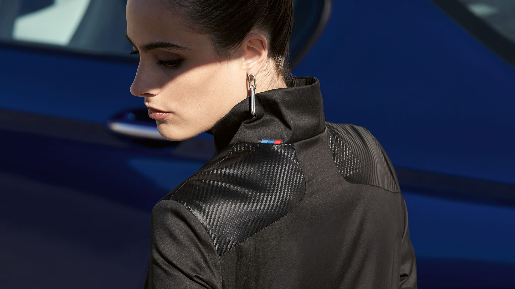 Dámská bunda BMW M. Na obrázku je žena oblečená do dámské bundy BMW M z kolekce BMW M. Detail kombinace materiálů.