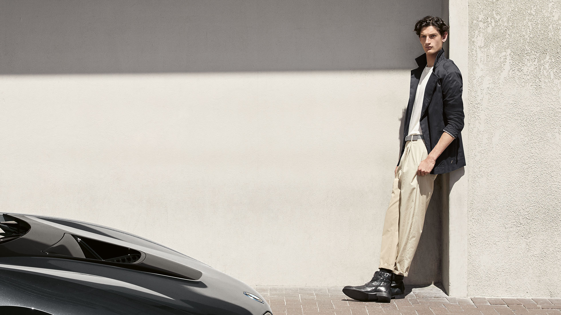 Kolekce BMW i. Na obrázku je muž opírající se o zeď v pánské bundě BMW i Jacket z kolekce BMW i Collection.