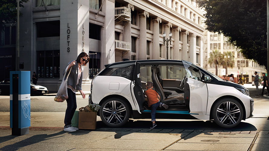 BMW i3 proti městskému pozadí BMW dojezd BMW i3 proti městskému pozadí s ženou a dítětem