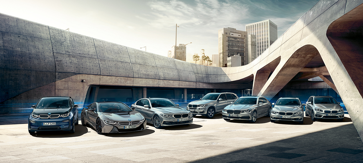 Elektrické a plug-in hybridní modely BMW před budovami Možnosti elektromobily BMW, elektrické a plug-in hybridní modely BMW před budovami