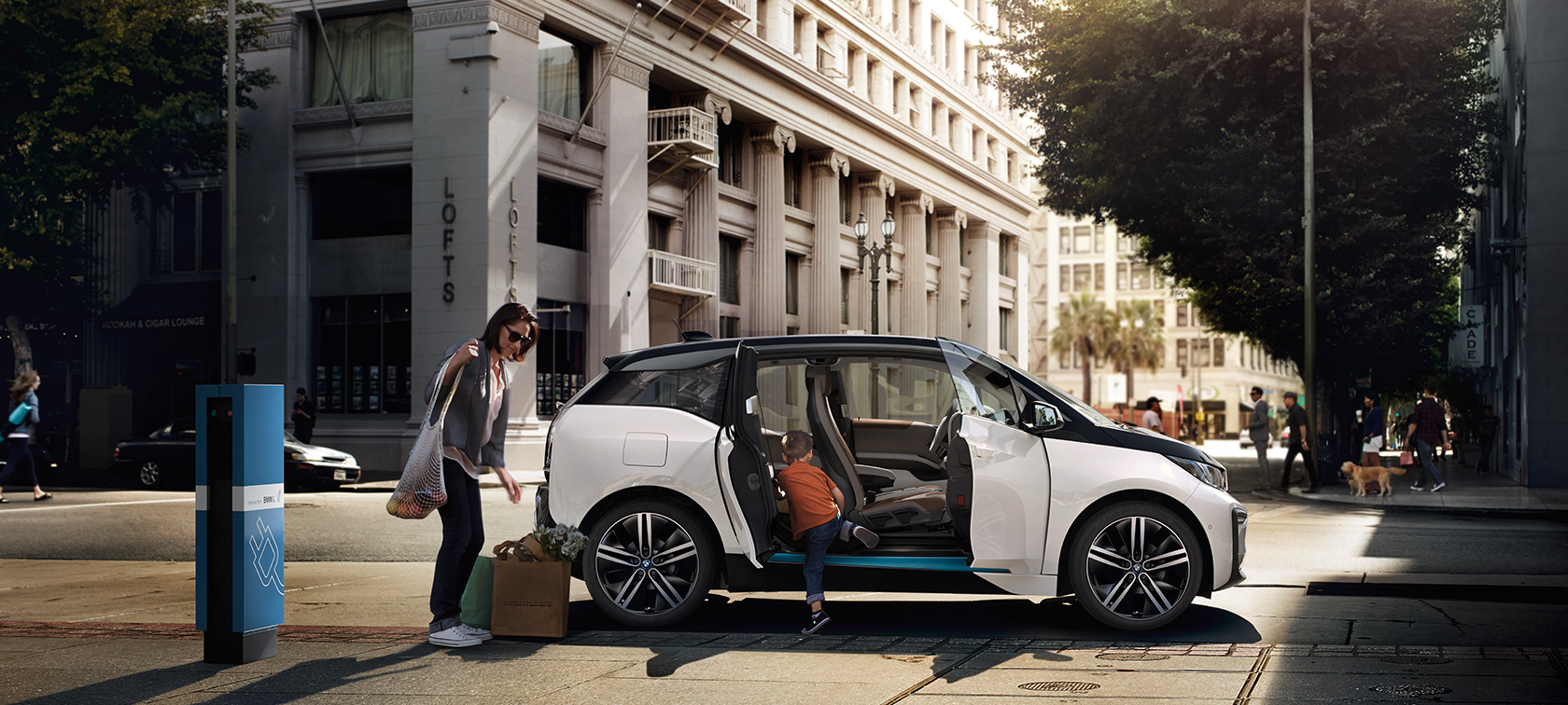 BMW i3 proti městskému pozadí BMW dojezd BMW i3 proti městskému pozadí s ženou a dítětem