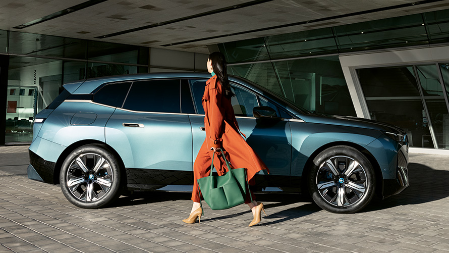 BMW Digitální klíč Výhody BMW Digitální klíč Výhody BMW iX i20 Pohled z boku s ženou v popředí