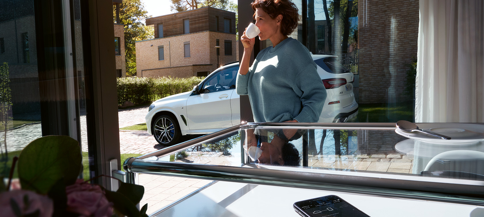 BMW Remote Software Upgrade Žena pije z šálku, zatímco BMW Remote Software Upgrade aktualizuje software jejího BMW X5
