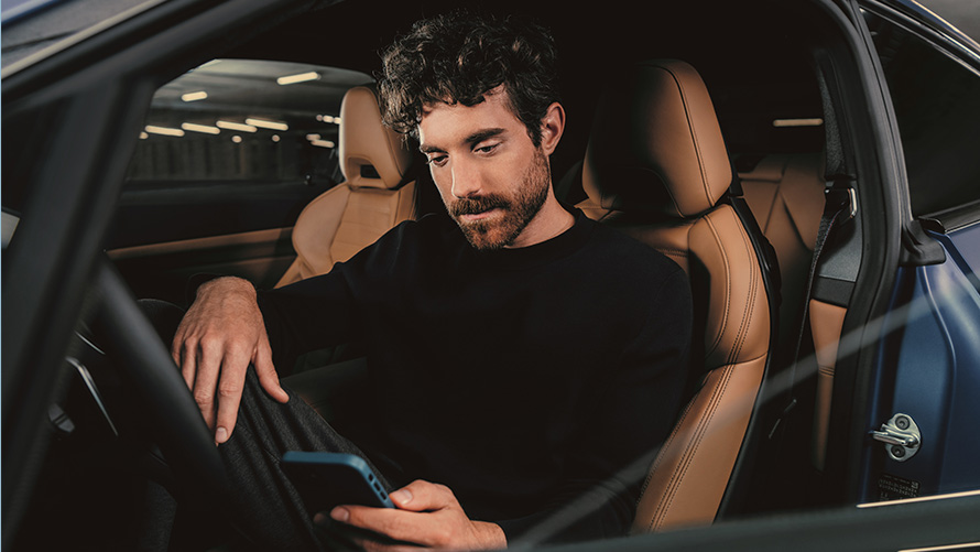 Muž sedící v BMW Muž sedící v BMW se dívá do svého telefonu