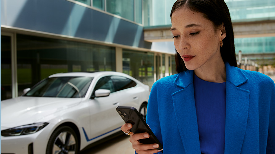 Žena stojí před BMW Žena stojí před BMW a dívá se do svého telefonu