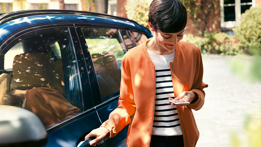 BMW Teleservices Žena s chytrým telefonem stojí před dveřmi svého BMW