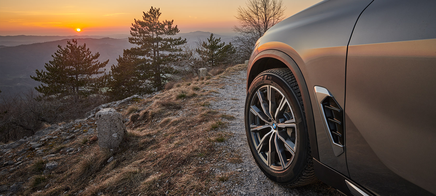 BMW Originální kola a pneumatiky na BMW X5 (G05 LCI) na nezpevněné cestě u pohoří směrem k západu slunce BMW Originální kola a pneumatiky na BMW X5 (G05 LCI)