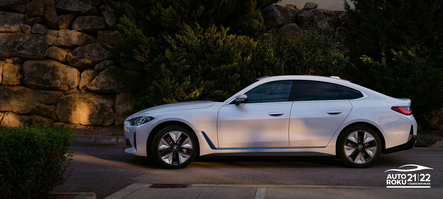 BMW i4 eDrive40 G26 2021 Mineral White tř&iacute;čtvrtečn&iacute; pohled zepředu stoj&iacute;c&iacute; před jezerem s kopcem v pozad&iacute;
