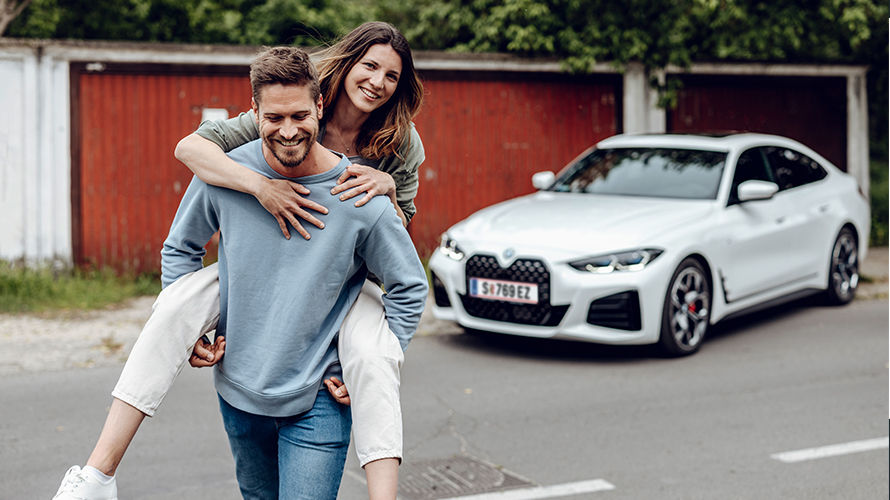Smějící se muž odchází od BMW i4 a za ním jde usměvavá žena. Smějící se muž odchází od BMW i4 a za ním jde usměvavá žena.