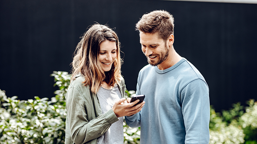Muž a žena se dívají do jejího telefonu. Muž jí něco ukazuje na displeji. Muž a žena se dívají do jejího telefonu. Muž jí něco ukazuje na displeji.