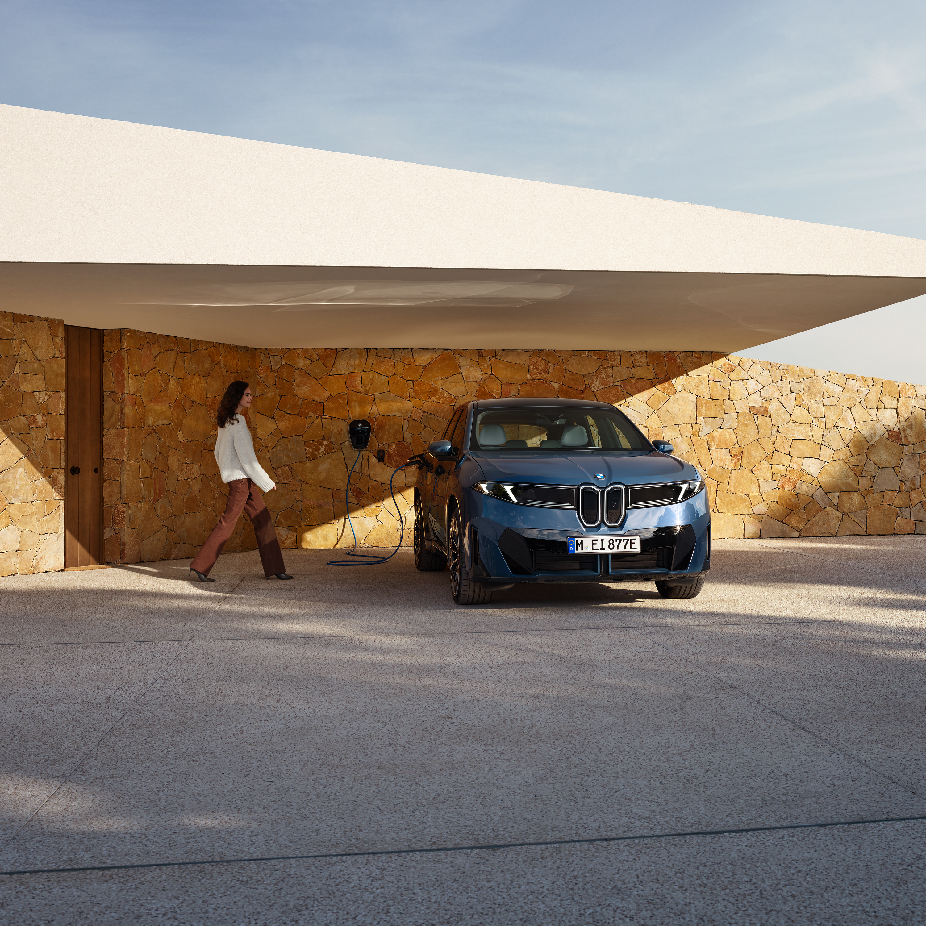 Žena jde směrem k BMW iX3 připojenému k wallboxu
