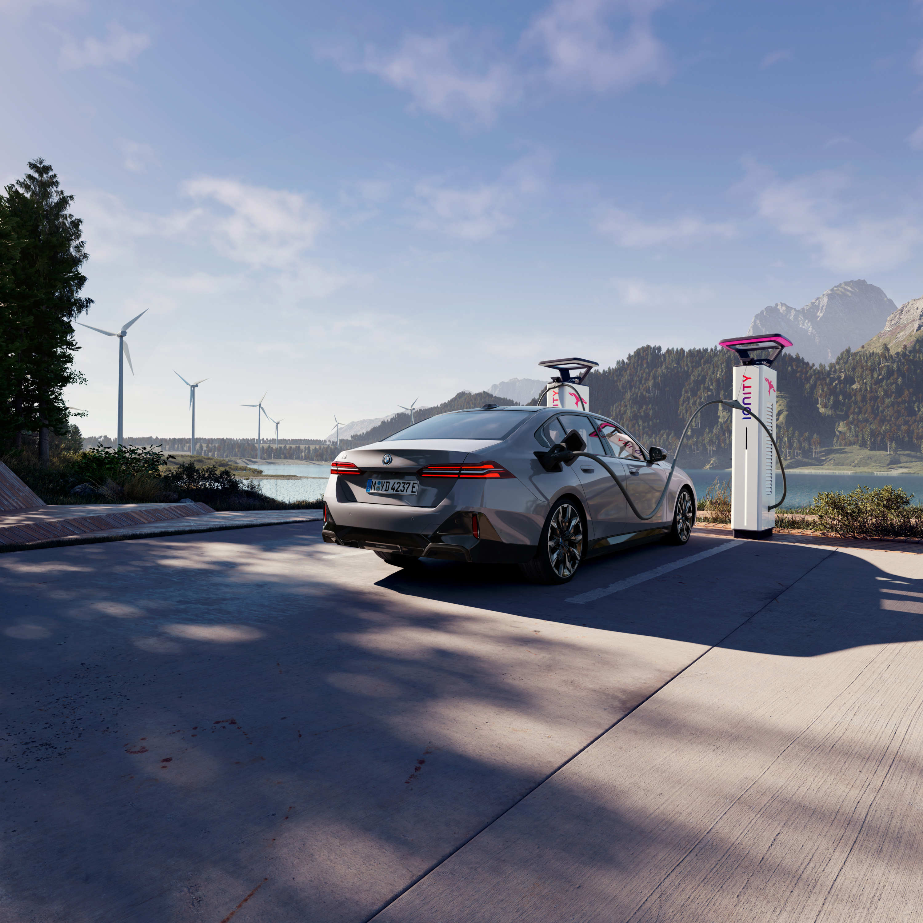 Nabíjející se BMW na nabíjecím místě s výhledem na vodu, hory a větrné elektrárny