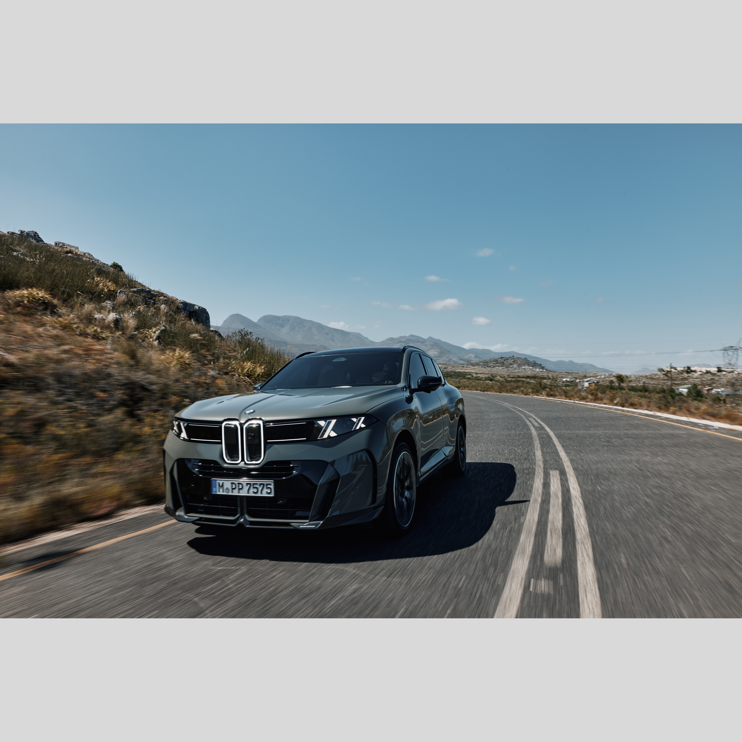 BMW iX5 jedoucí po klikaté horské silnici při západu slunce